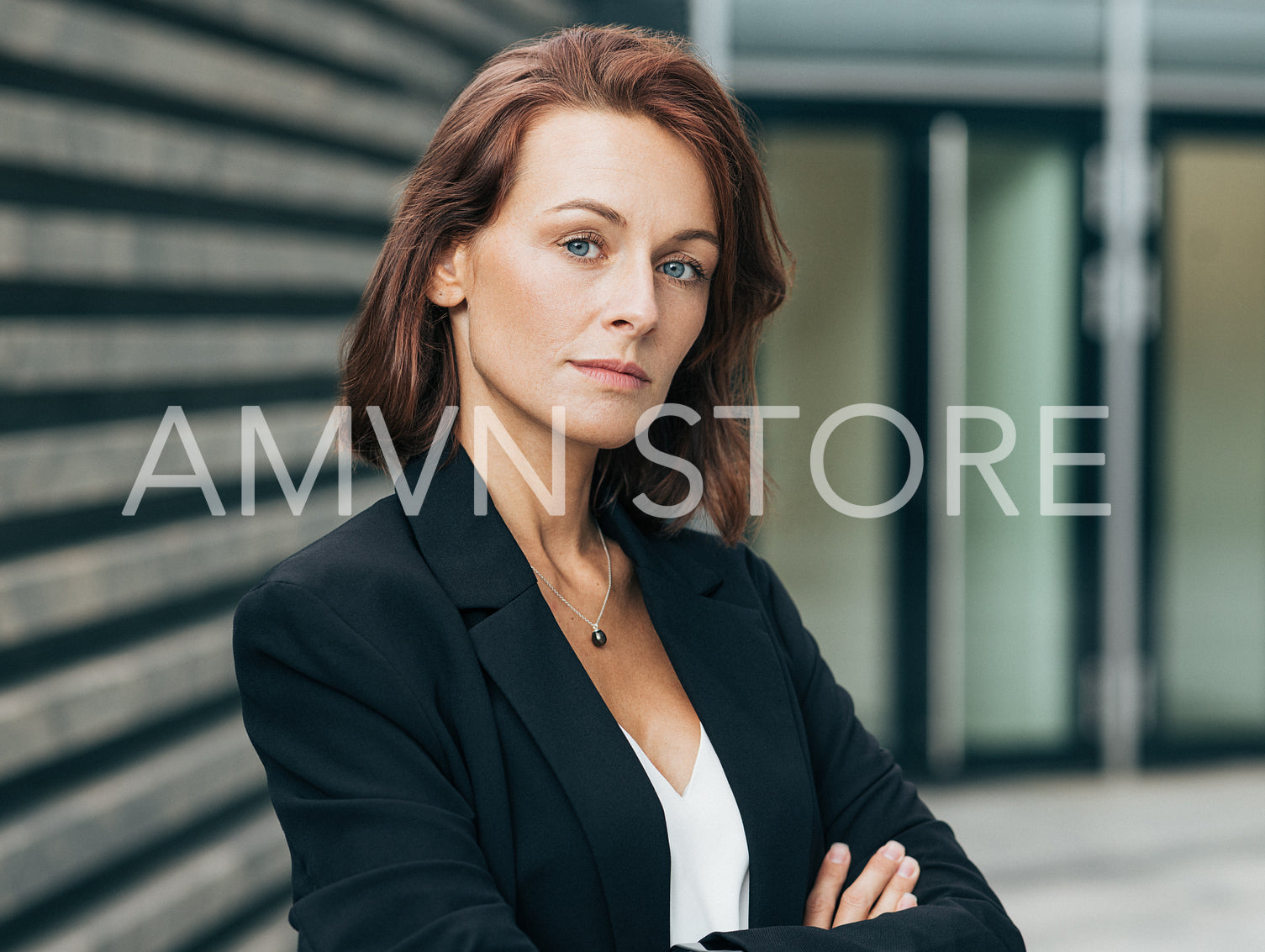 Portrait of a confident female with ginger hair standing with crossed arms looking straight to camera. Close-up portrait of a corporate person.