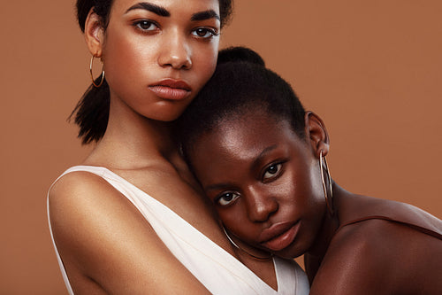 Two beautiful women standing in studio and looking at camera. Young woman relaxing on girlfriend's chest.