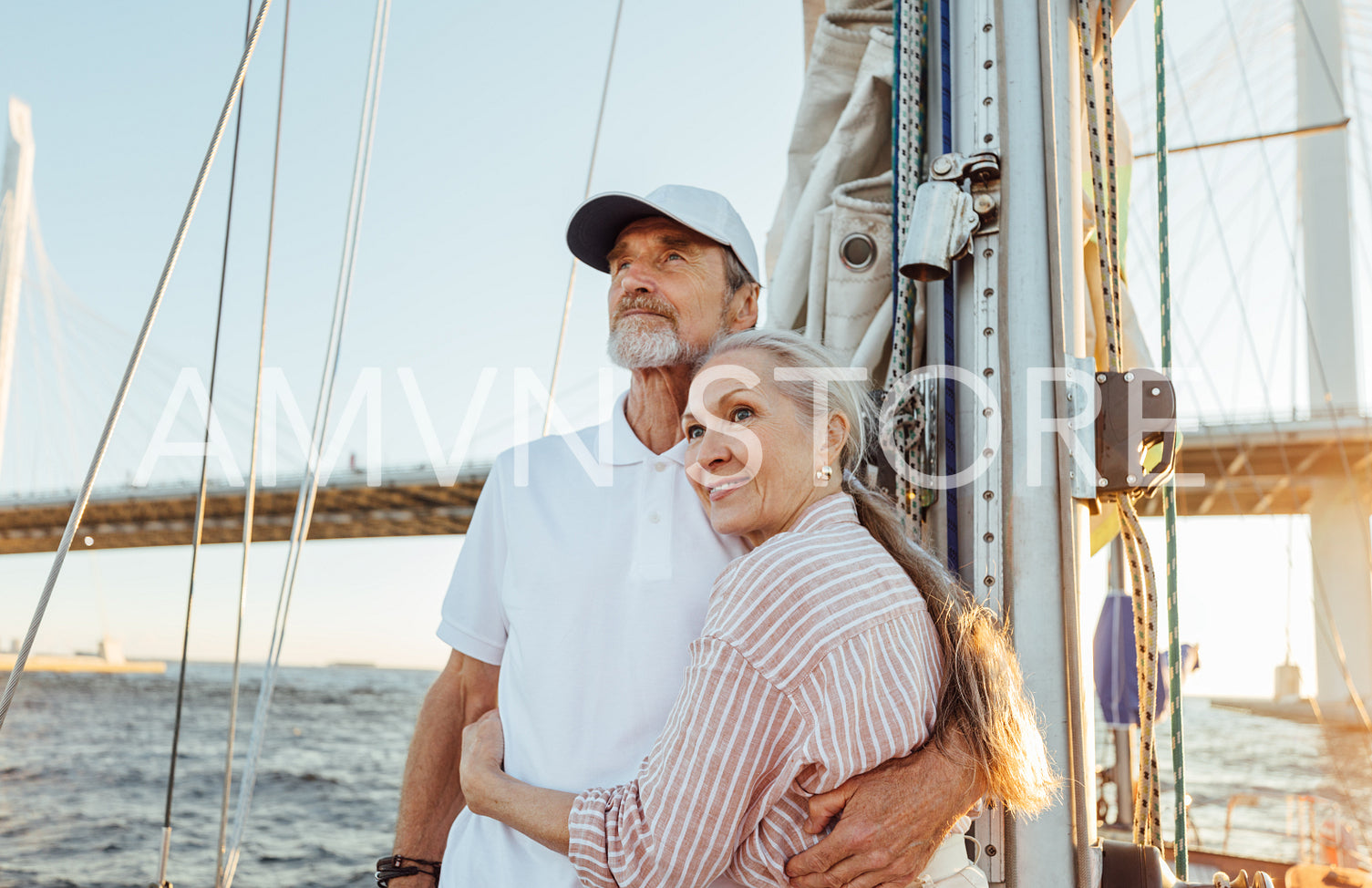 Affectionate senior couple hugging together and looking into the distance while standing on a yacht	