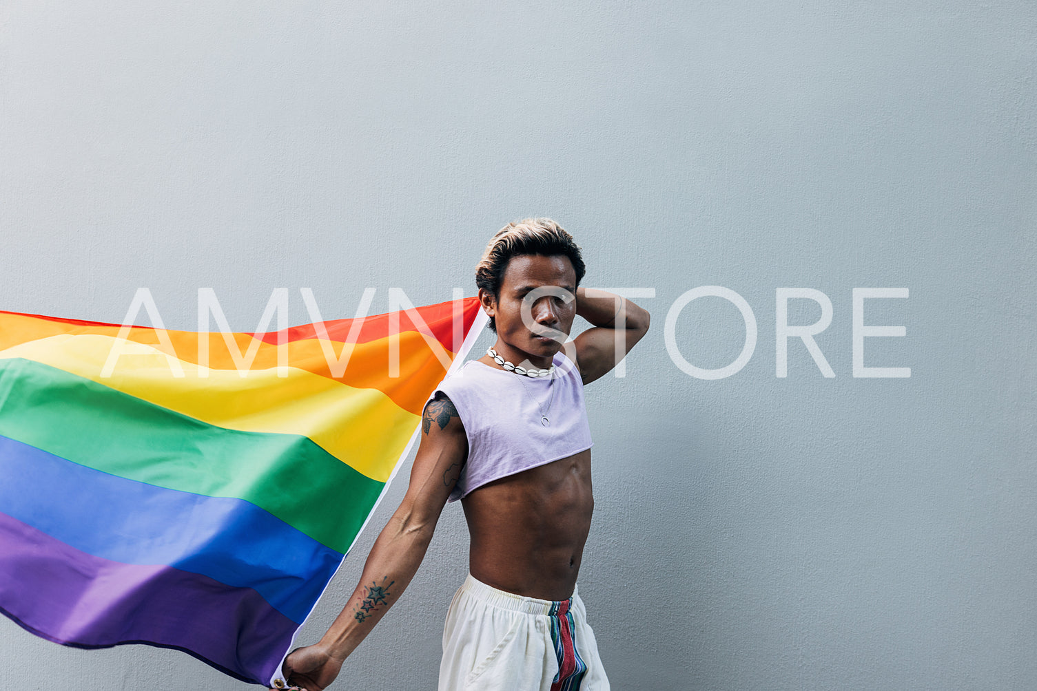 Young man with rainbow flag looking at camera outdoors