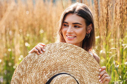 Smiling woman standing outdoors with big straw hat surrounded by tall grass