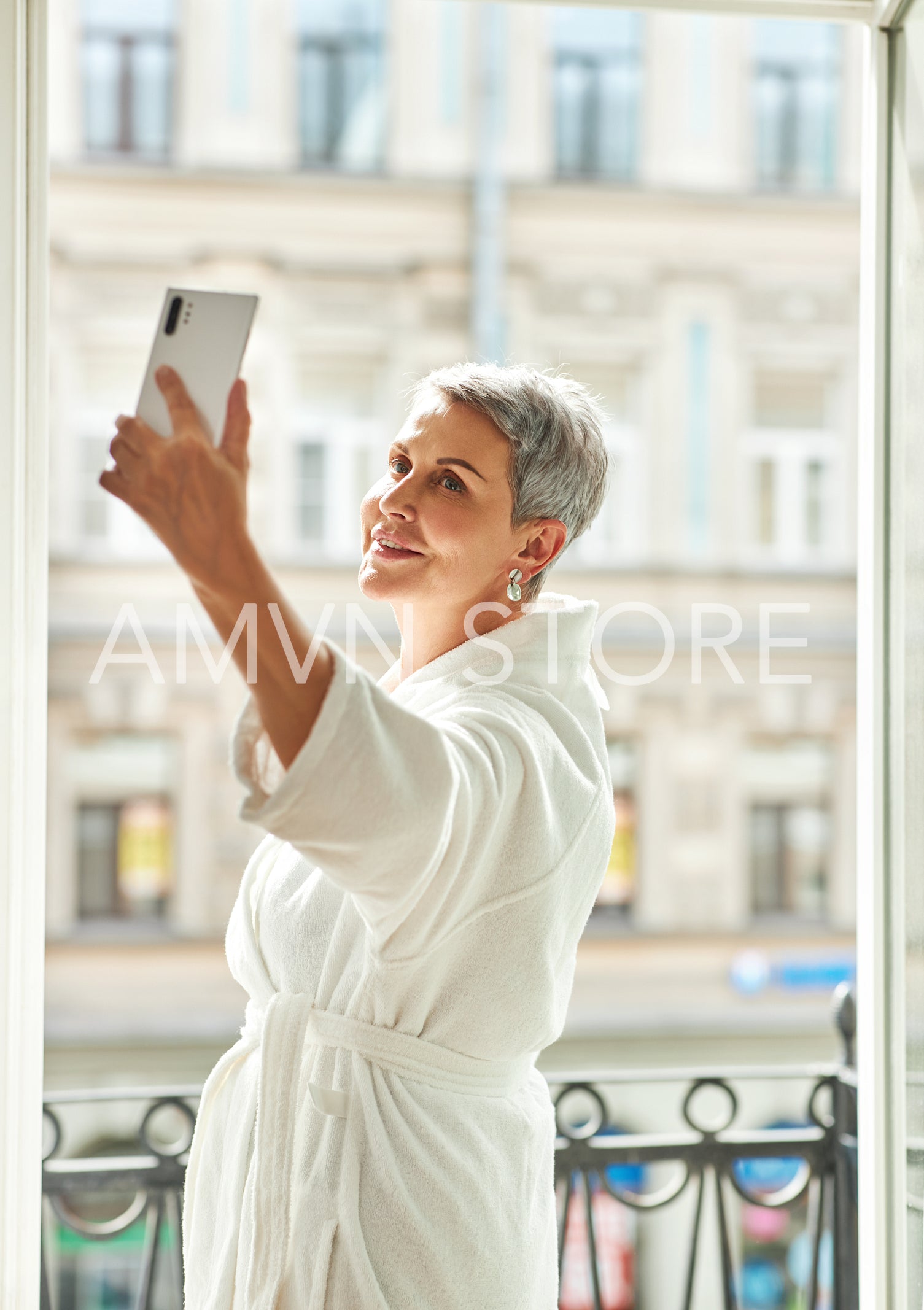 Senior woman wearing bathrobe holding a smartphone at hotel room	