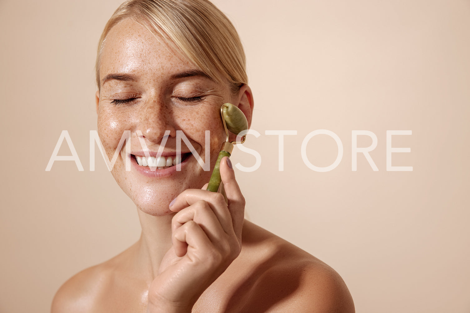 Smiling woman with freckles using jade stone roller against pastel background