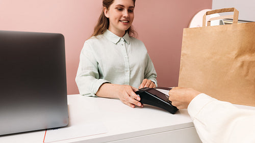 Smiling boutique owner holding pos terminal while customer makin