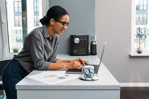 Side view of smiling woman working with laptop on kitchen counter at home