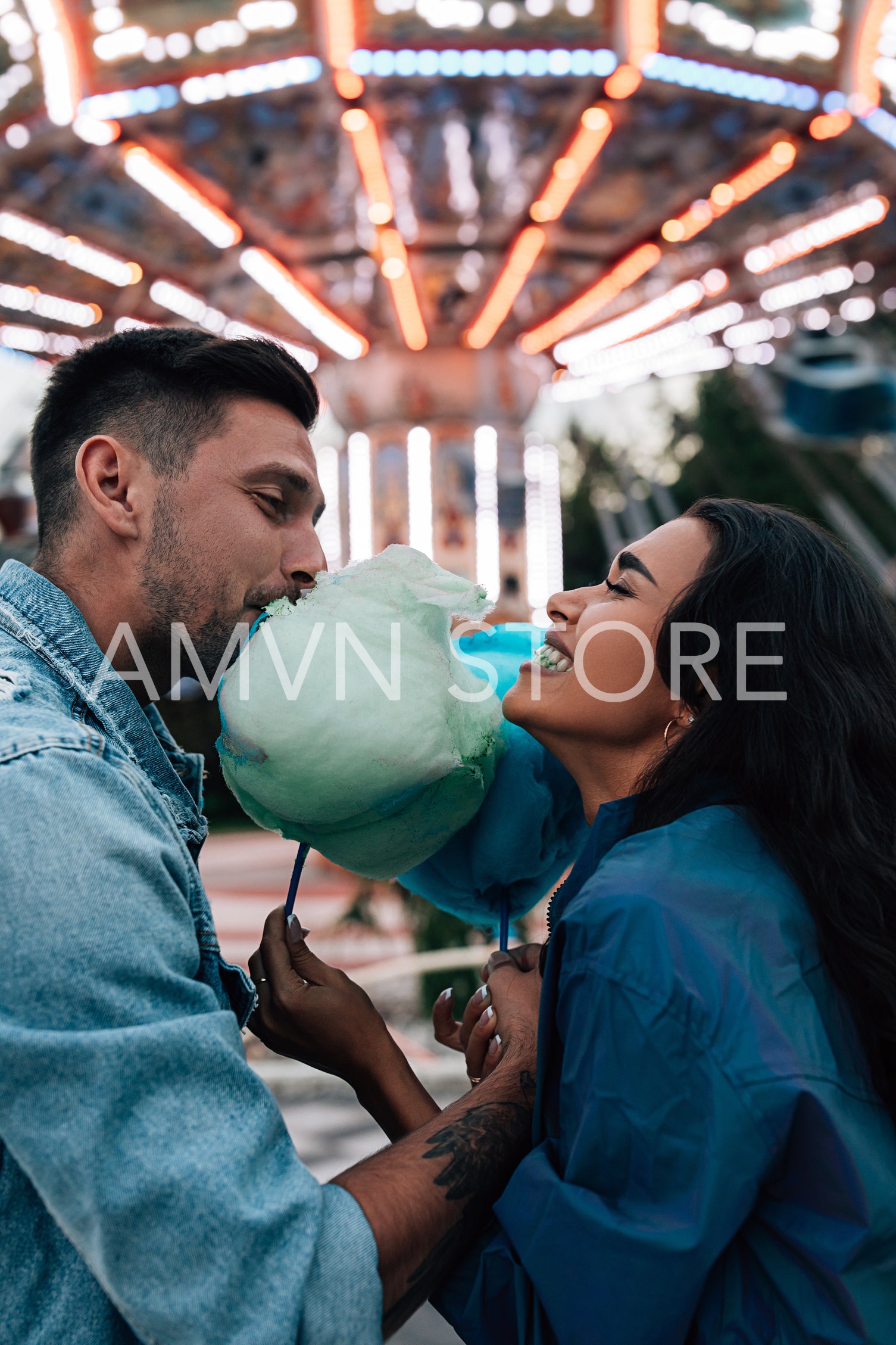 Young happy couple biting a cotton candy in the evening in an amusement park