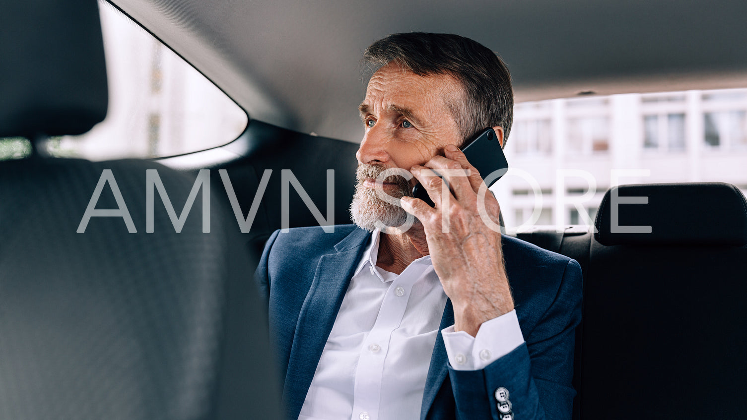 Serious businessman talking on cell phone sitting in taxi on backseat	