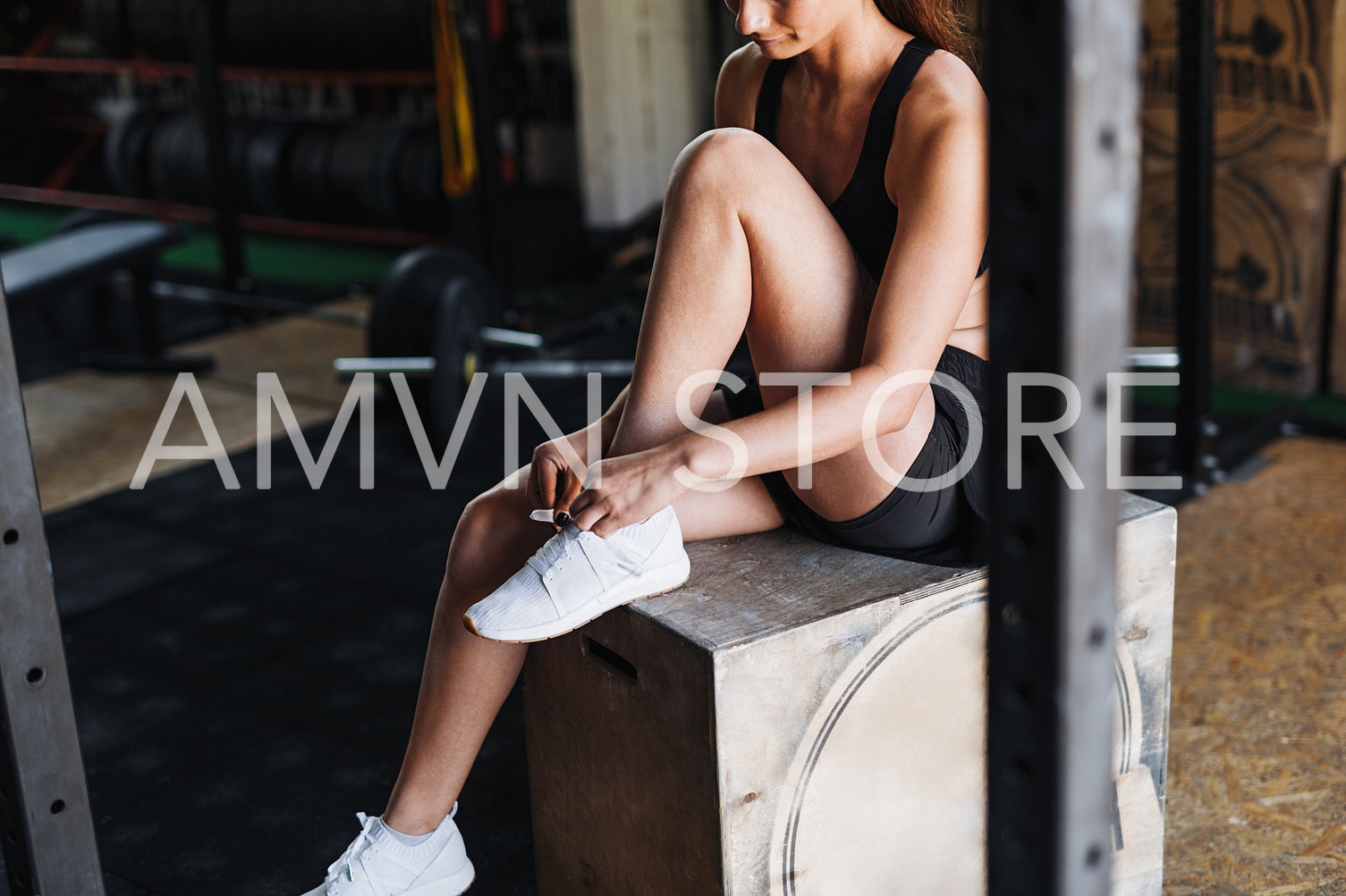 Unrecognizable woman sitting in gym tying shoelaces on sneakers	