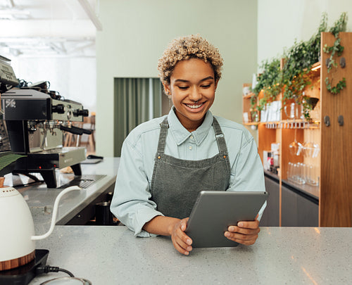 Young smiling barista holding a digital tablet at bar counter. Female entrepreneur in an apron with digital tablet in her cafe.