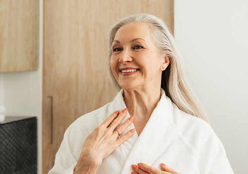 Happy senior woman looking at her reflection in the mirror in morning in the bathroom