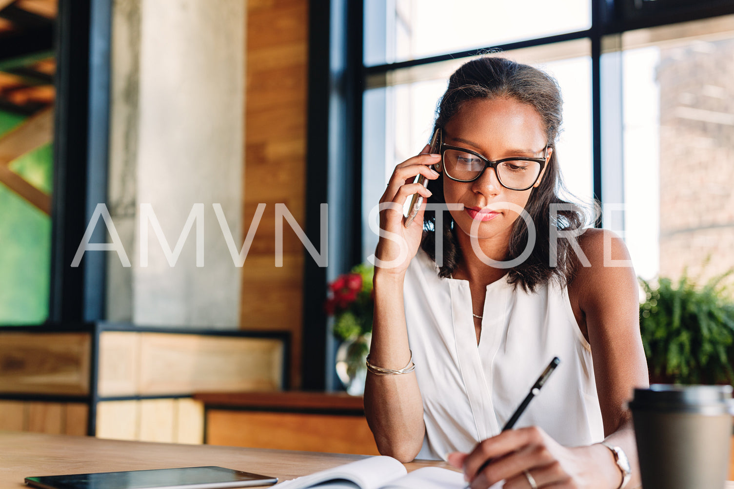 Businesswoman taking notes while talking on her smartphone in cafe	