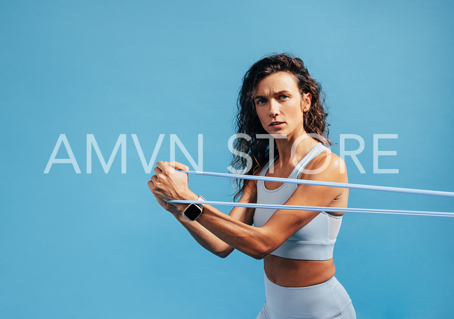 Portrait of young fitness female training with resistance band on blue background