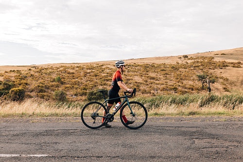 Side view of young professional cyclist walking with her road bike on countryside