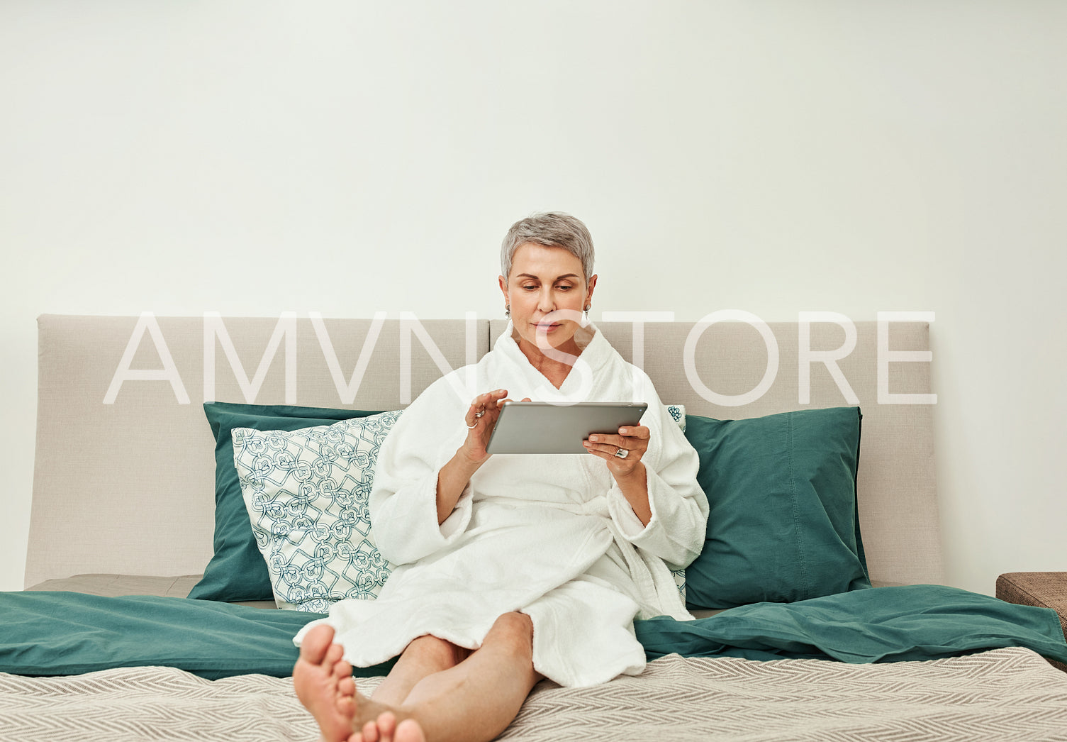 Adult female in bathrobe lying on a bed using a digital tablet