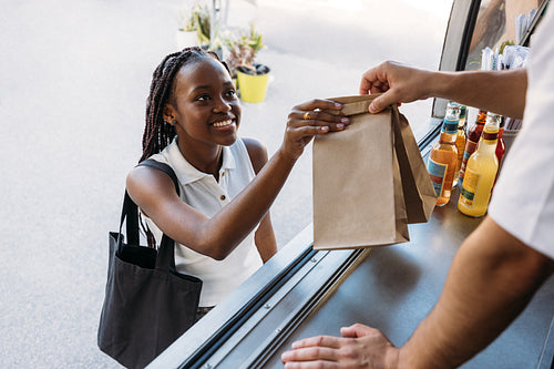 Young cheerful woman receiving takeaway food from a salesman. Unrecognizable food truck owner giving packaged food to a client.