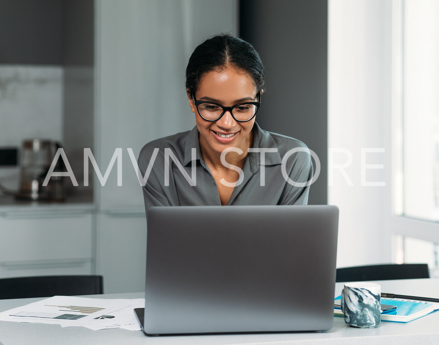 Smiling female in eyeglasses working on a laptop at the kitchen counter