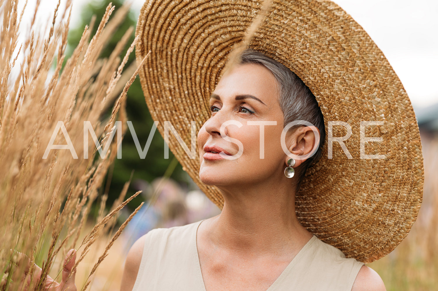 Close-up mature female with short grey hair wearing a straw hat looking at wheat