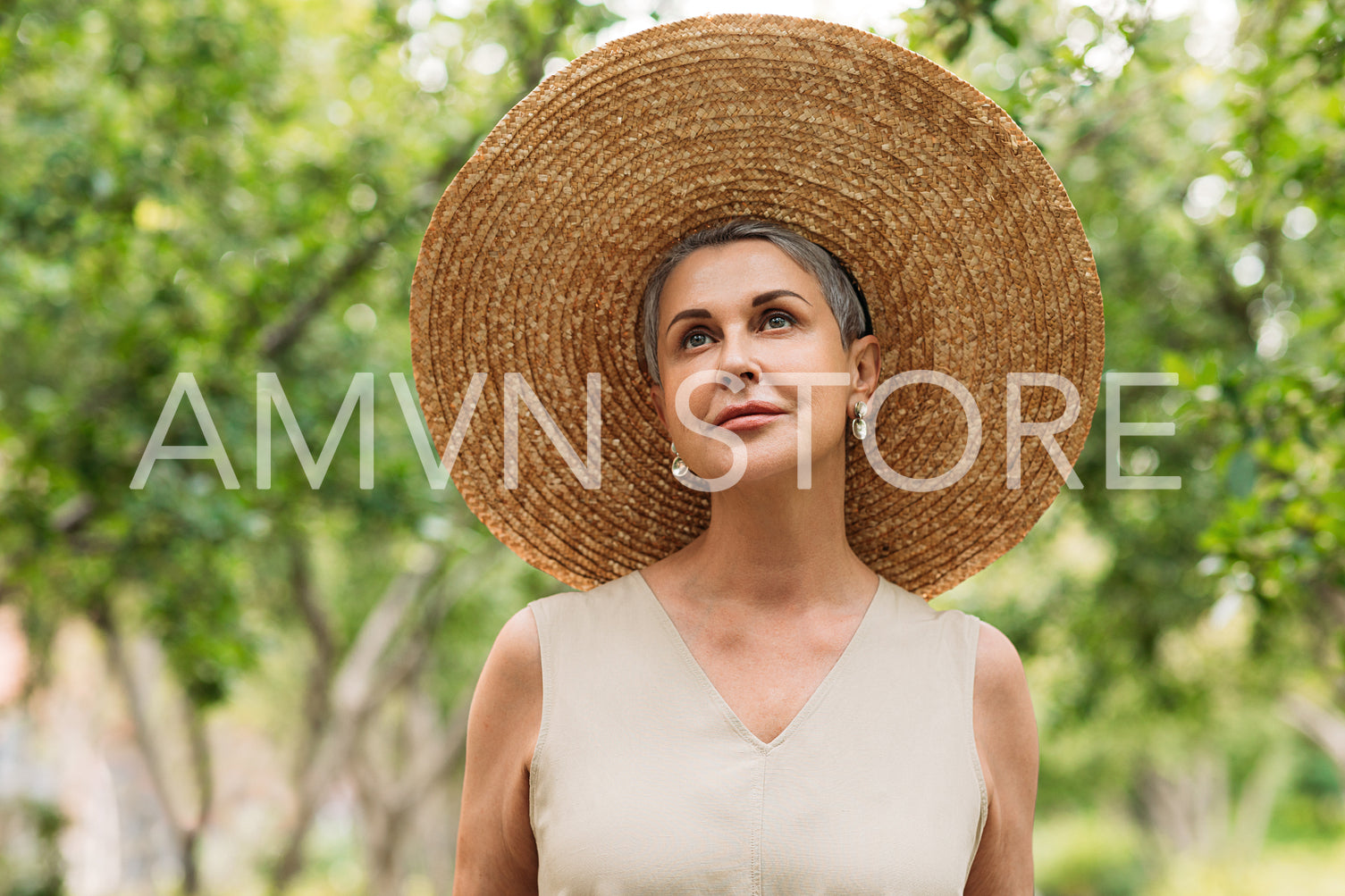 Senior stylish woman in a straw hat standing in the park and looking up