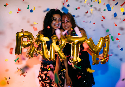 Two happy girls standing near a wall under confetti