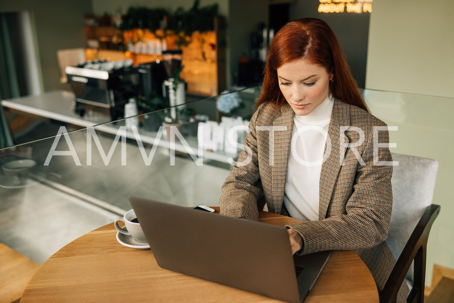 Beautiful businesswoman with ginger hair typing on a laptop while sitting at a table in a coffee shop