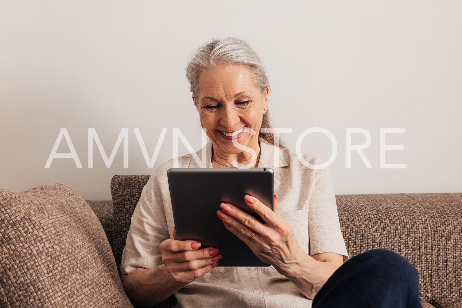 Close up of a smiling senior woman with grey hair holding digital tablet while sitting on couch