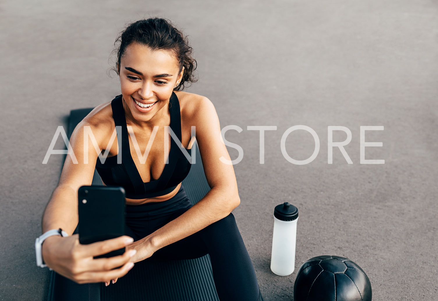 Smiling sportswoman live streaming from her cell phone while sitting on a mat outdoors	