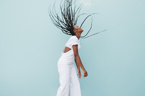 Side view of a young female with braided hair flying in air at the blue wall