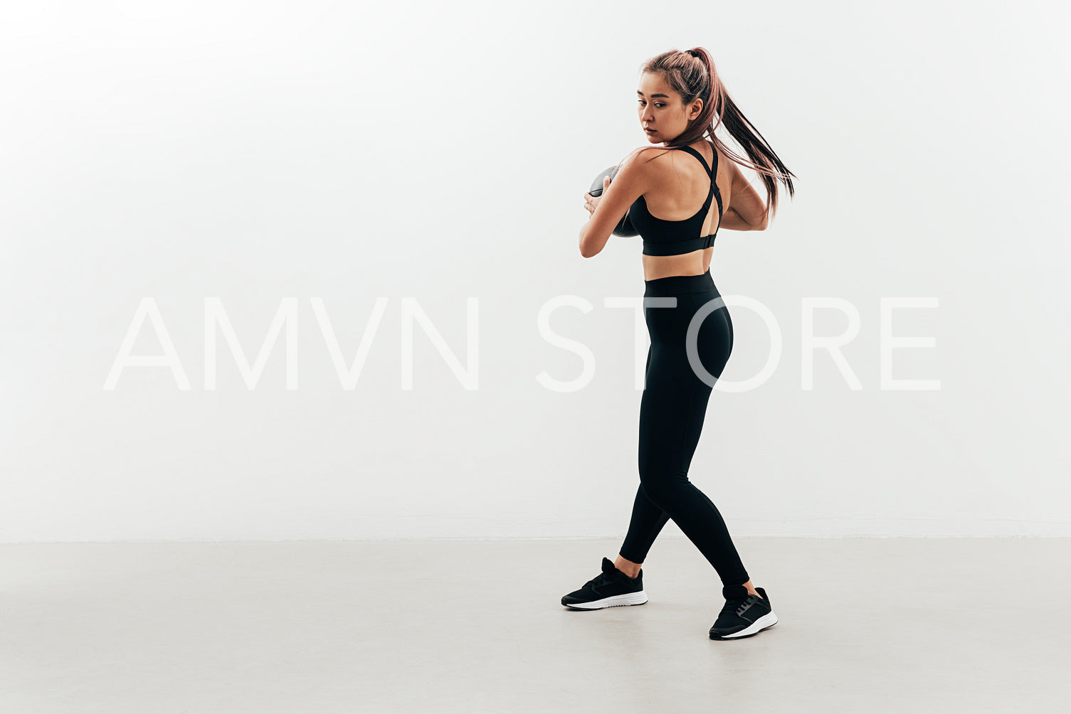 Young muscular woman doing exercises with a medicine ball against a white wall