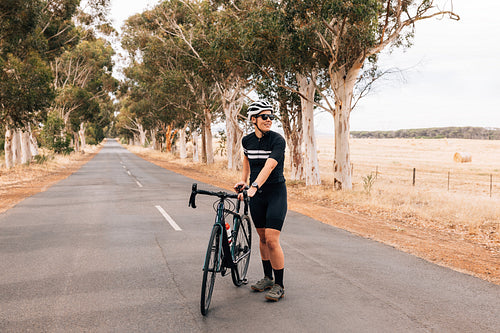 Professional woman cyclist standing with her bike on the centre of the countryside road