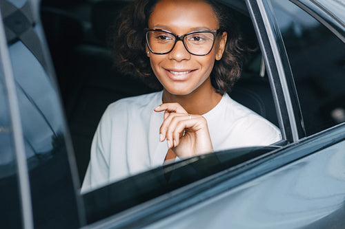 Smiling businesswoman sitting on a backseat of the taxi and looking away. Young entrepreneur in a car.