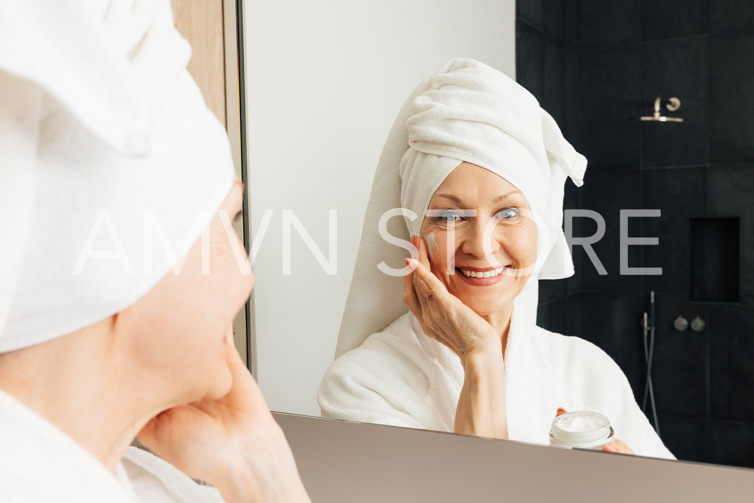 Portrait of a smiling senior woman applying facial treatment. Cheerful aged female with facial cream in bathroom.