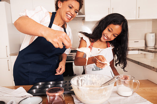 Girl and her grandmother are having fun while mixing dough in the kitchen. Smiling granny and a kid cooking together.