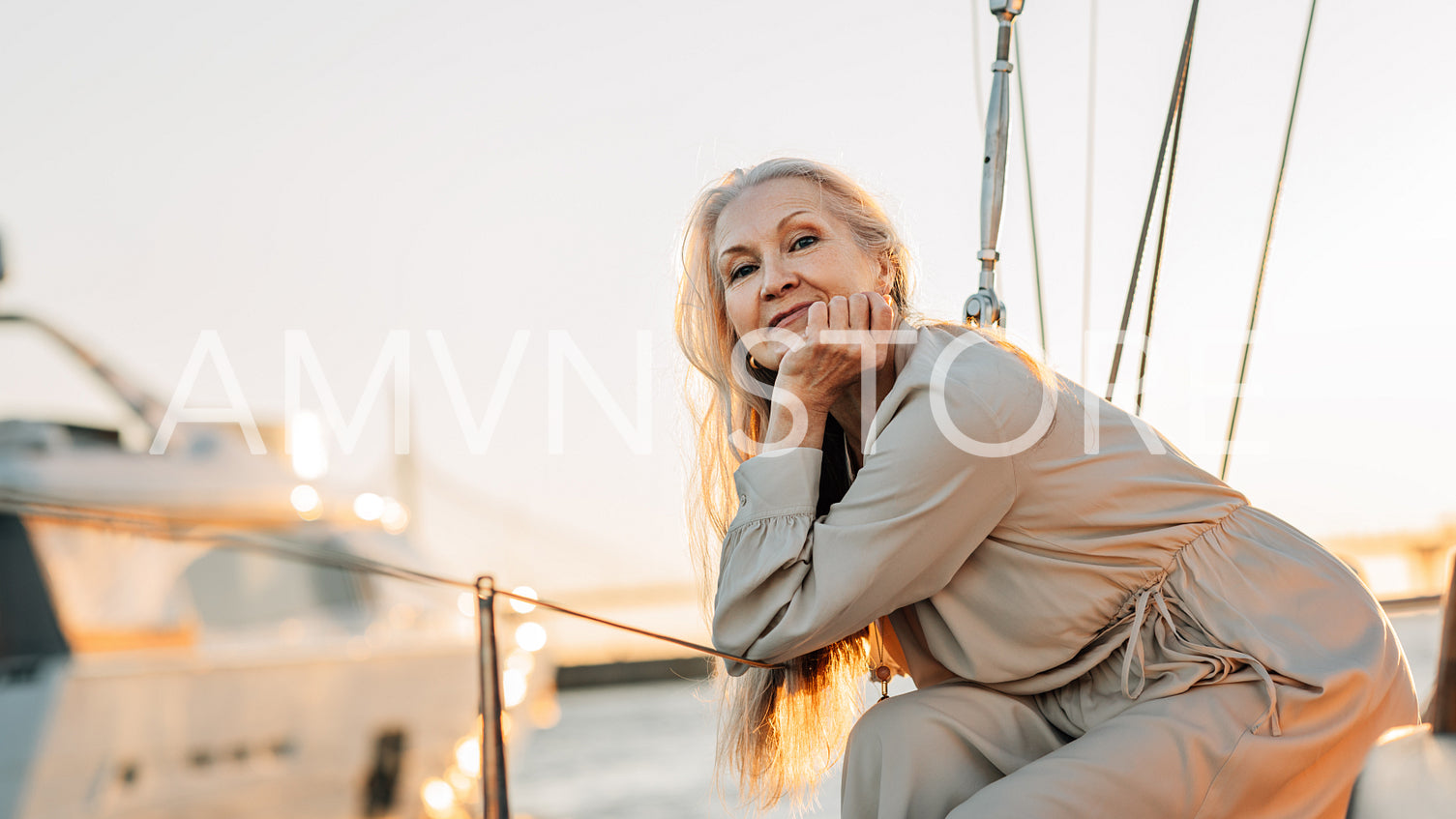 Portrait of a mature Caucasian woman with long grey hair looking straight to camera while sitting on a sailboat at sunset	