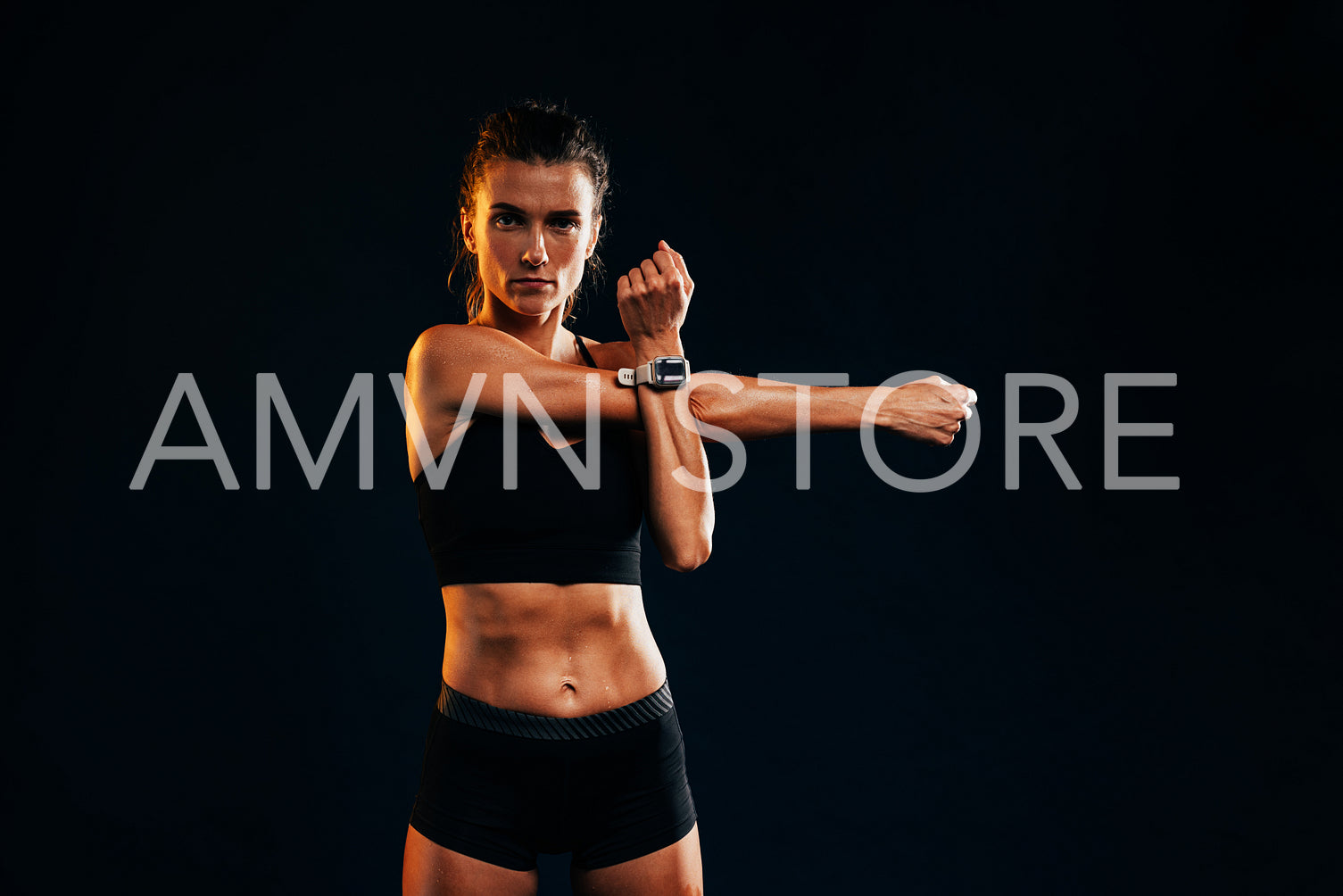 Young female doing warm up stretching workout on black background and looking at camera