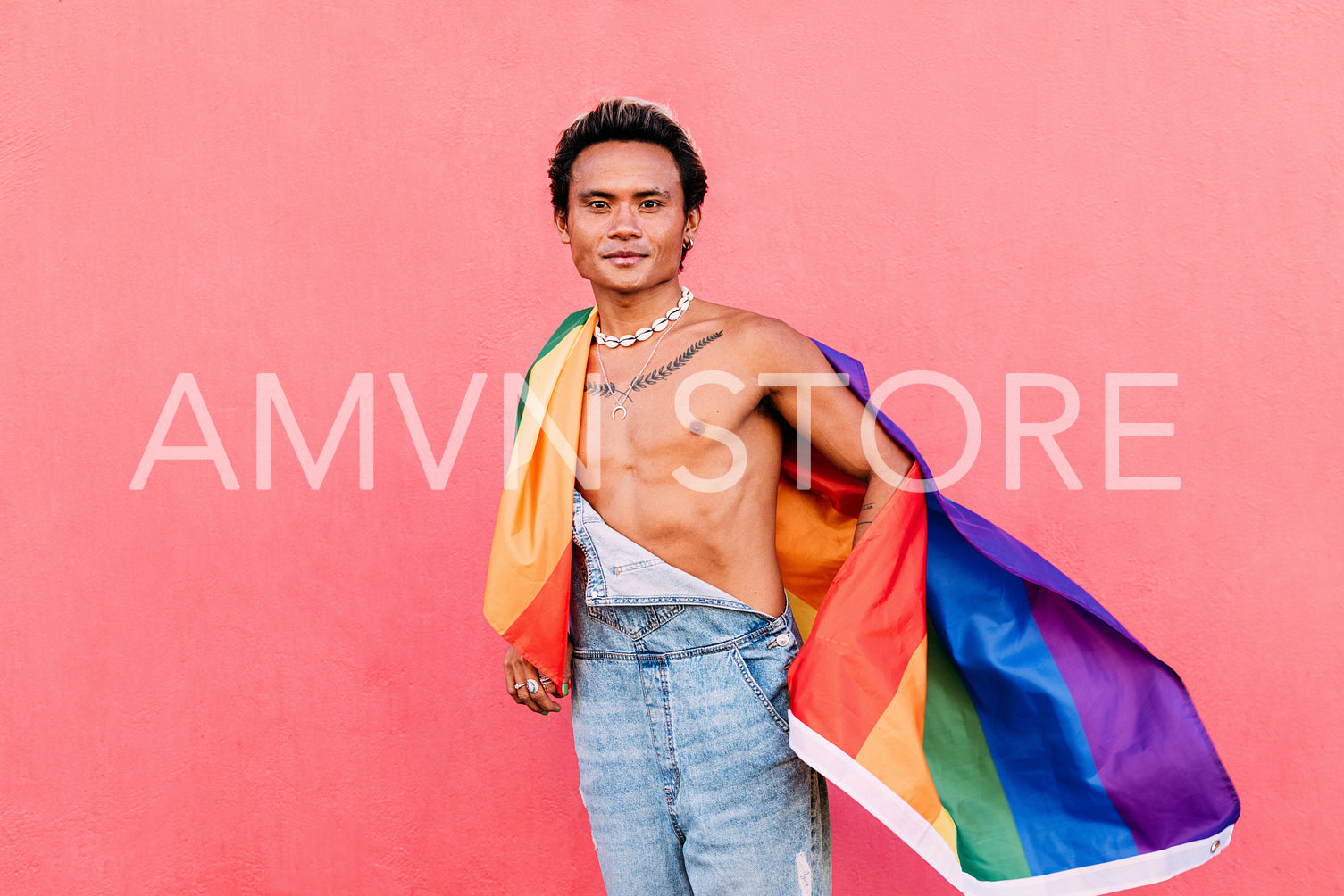 Young man wrapped in rainbow LGBT flag standing outdoors and looking at camera