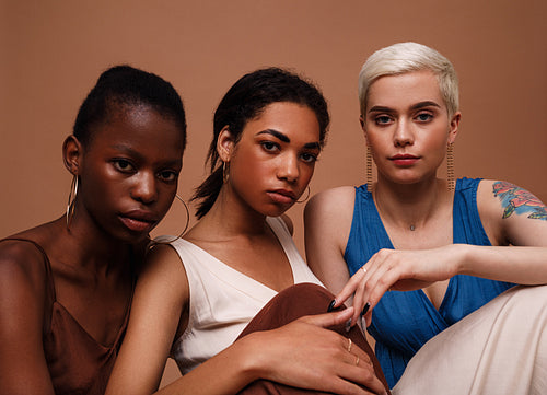 Three women in dresses sitting together against brown background