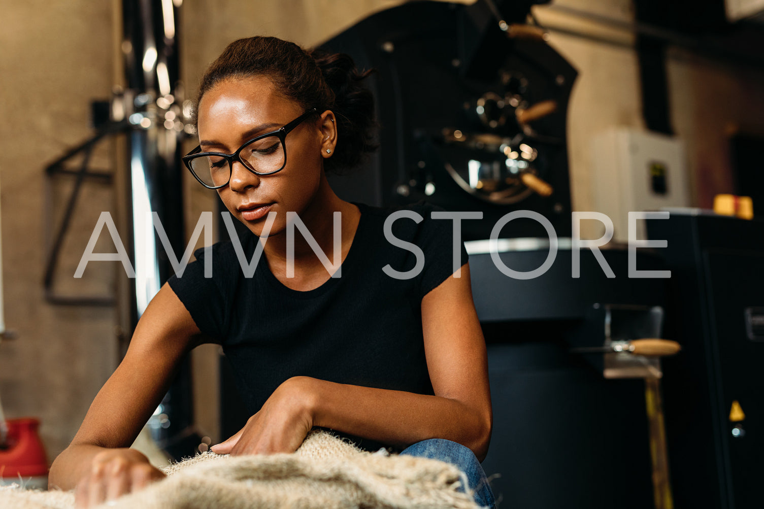 Young woman inspecting fresh coffee, sintting at sack in cafe	