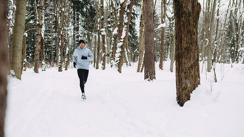 Young man exercising at winter, running through the forest