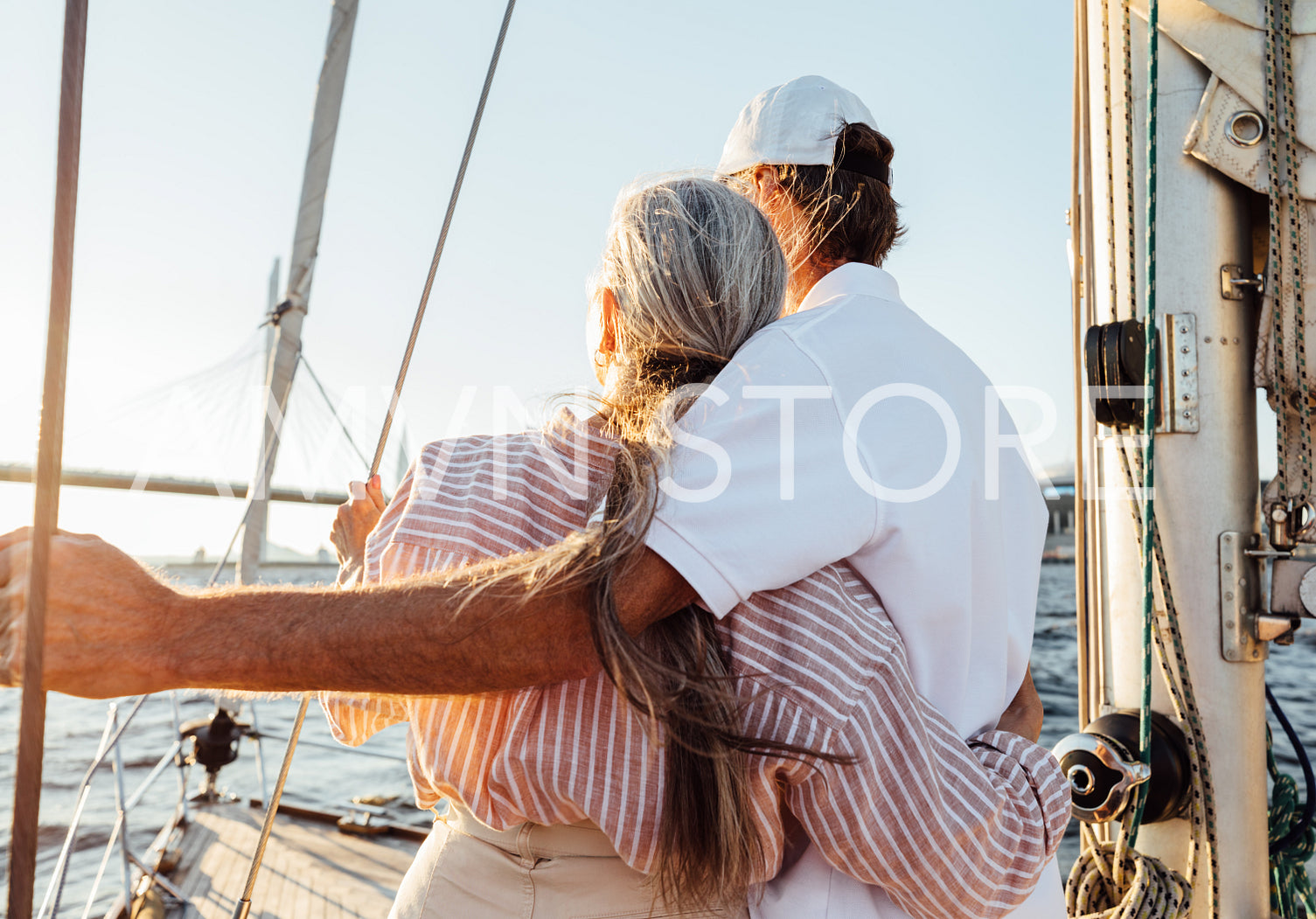 Back view of romantic elderly couple embracing on a sailboat and enjoying sunset. Two mature people standing on a yacht and hugging.	