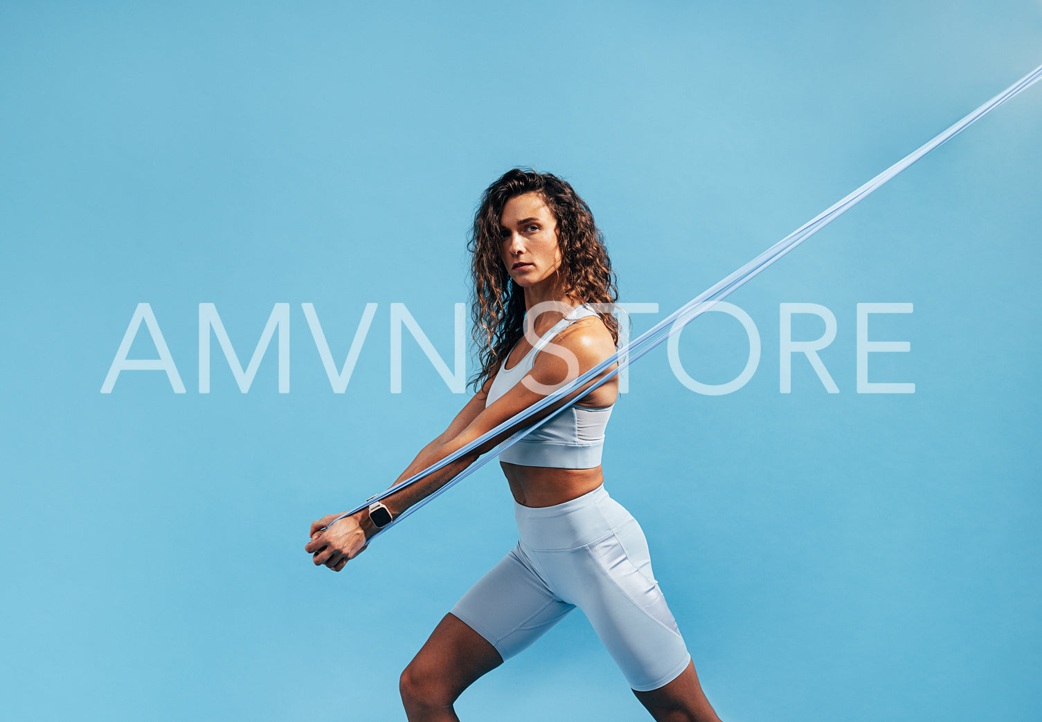 Strong and fit woman doing intense training with resistance band. Young female athlete exercising with stretching band on blue background.