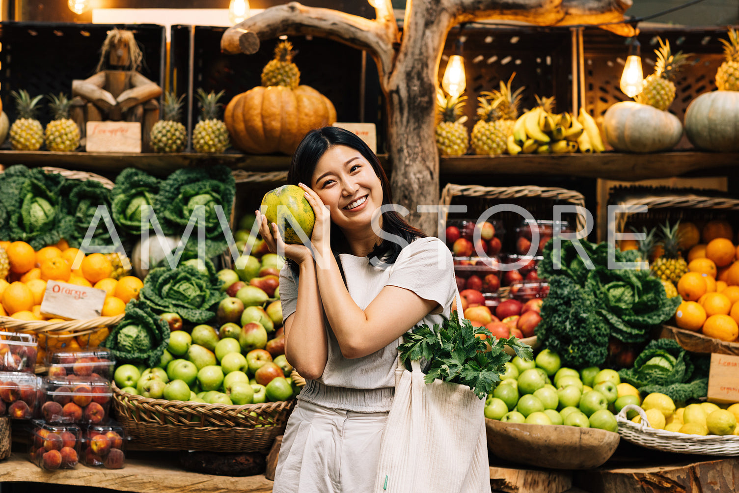 Portrait of a smiling Asian girl holding a fruit and looking at the camera. Young female with a bag at an outdoor market choosing fruits.