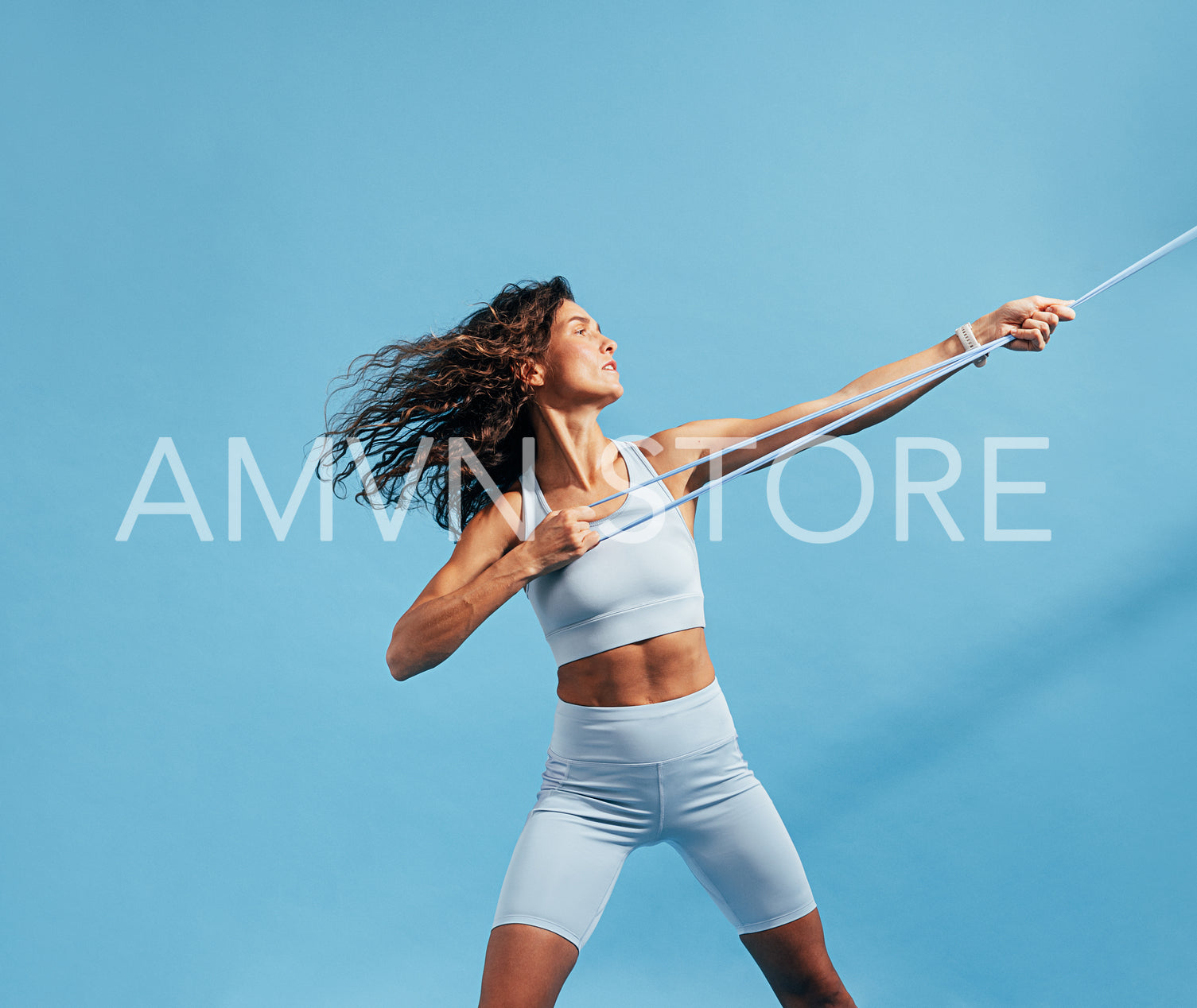 Woman in sportswear doing intense training with a resistance band. Slim female in sportswear exercising on blue background.