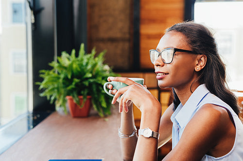 Woman sitting at cafe and looking away thinking with cup of coffee in hand