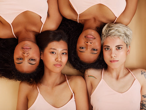 Group of four women lying together in a studio and looking at the camera. Diverse females lying head to head.