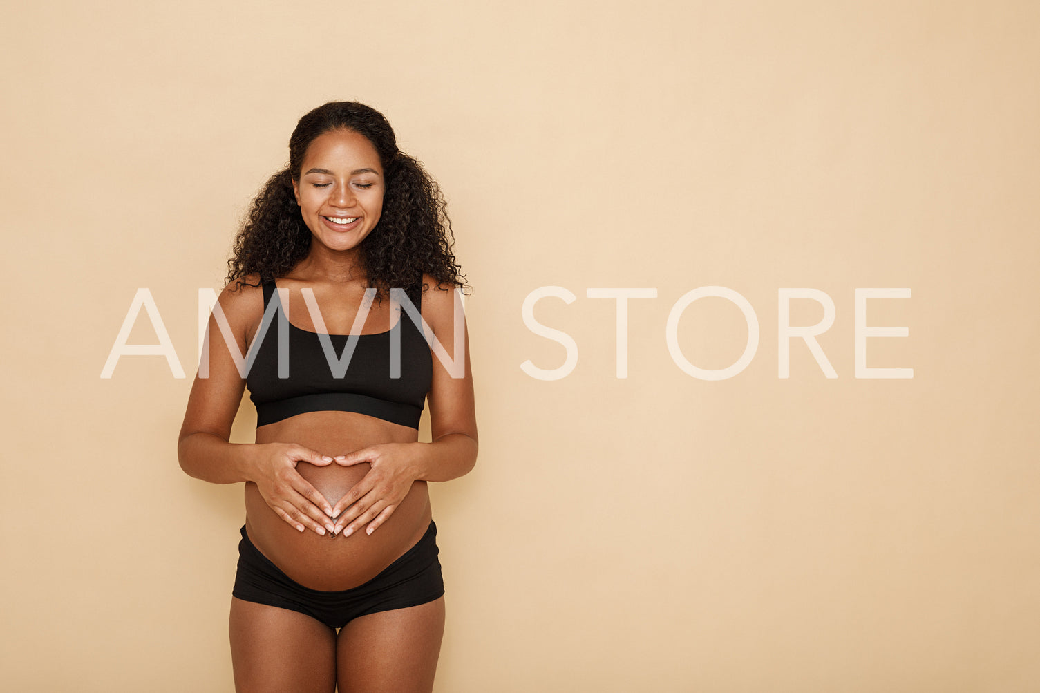 Pregnant woman holding hands on her belly making a heart symbol	