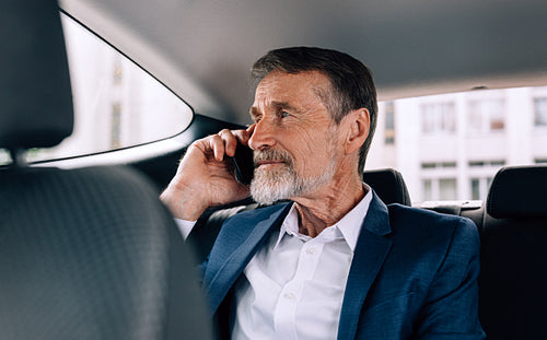 Pensive senior man holding a cell phone and looking on window while sitting in car