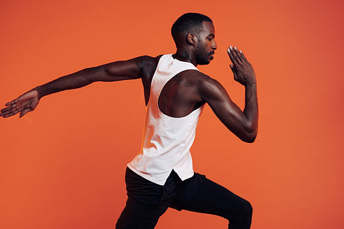 Close up of male runner exercising over an orange background. Young athlete sprinting in the studio.