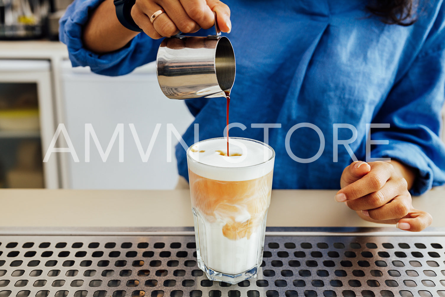 Cropped shot of female barista making a glass of latte while standing behind counter. Hands of woman pouring coffee into a cup milk.	