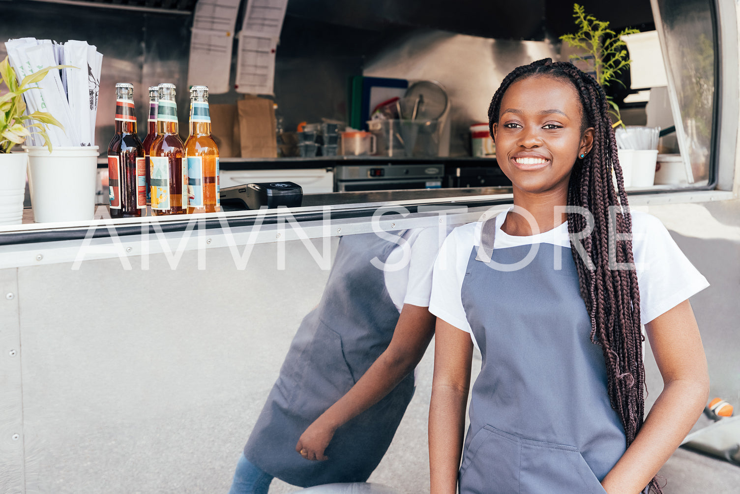 Smiling waitress with long braids leaning on food truck looking away