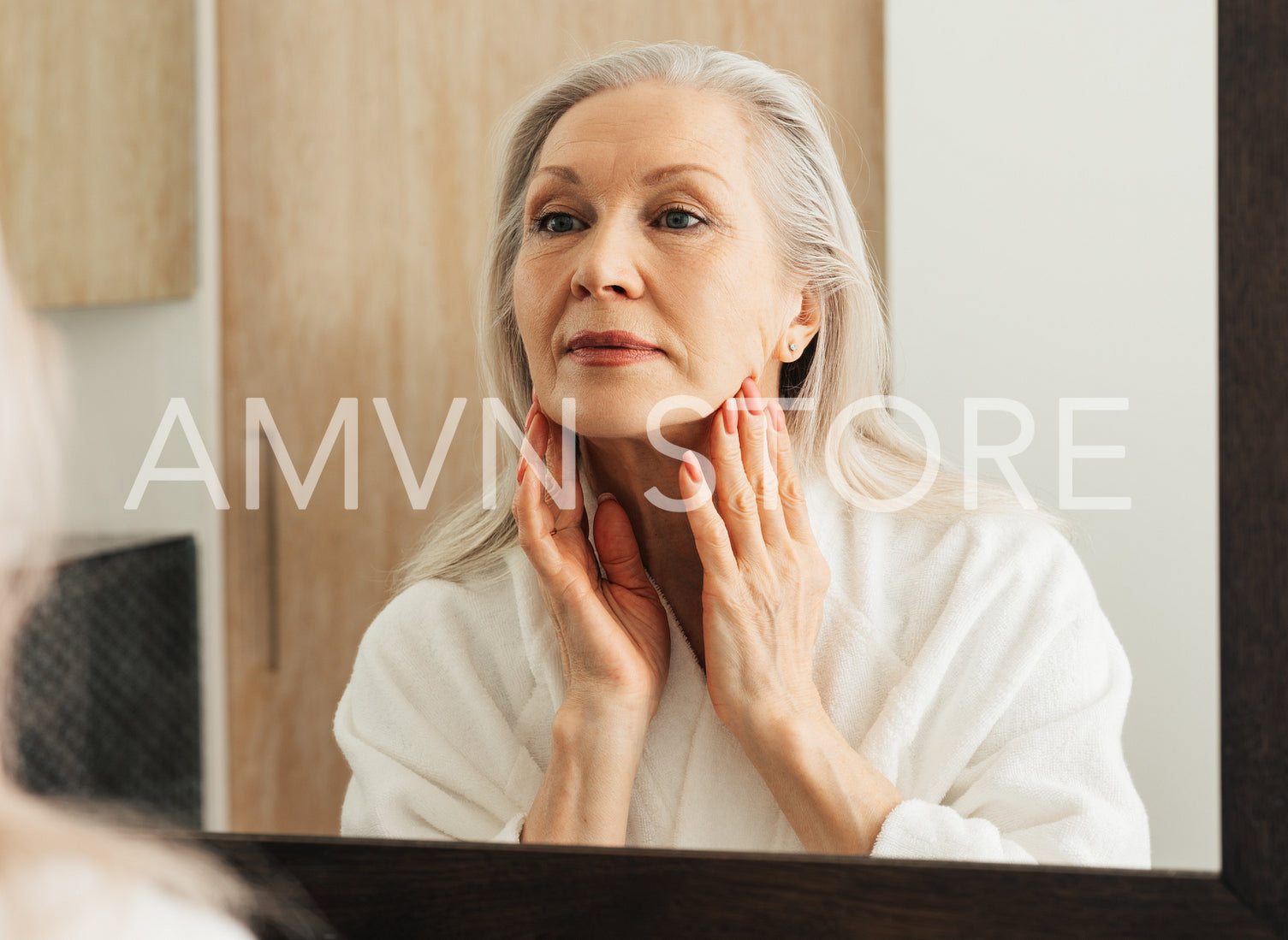 Senior woman stretching skin on her face in front of a mirror